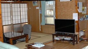 Un salón japonés tradicional con suelo de tatami, una mesa de madera baja, un sofá, un televisor y una puerta corredera shoji.