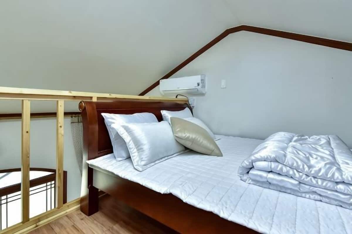A single bed with a wooden headboard, white bedding, and a window with a view.