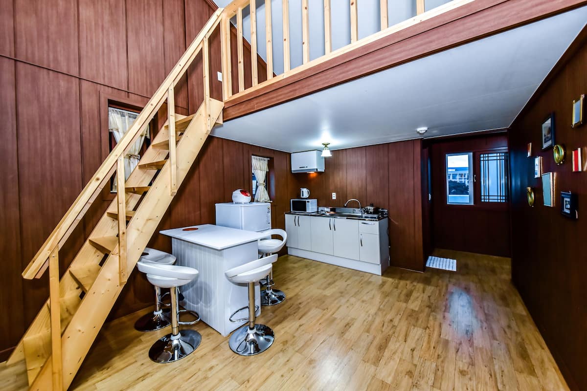 A compact kitchen with a wooden staircase, white cabinetry, and a small island with bar stools.