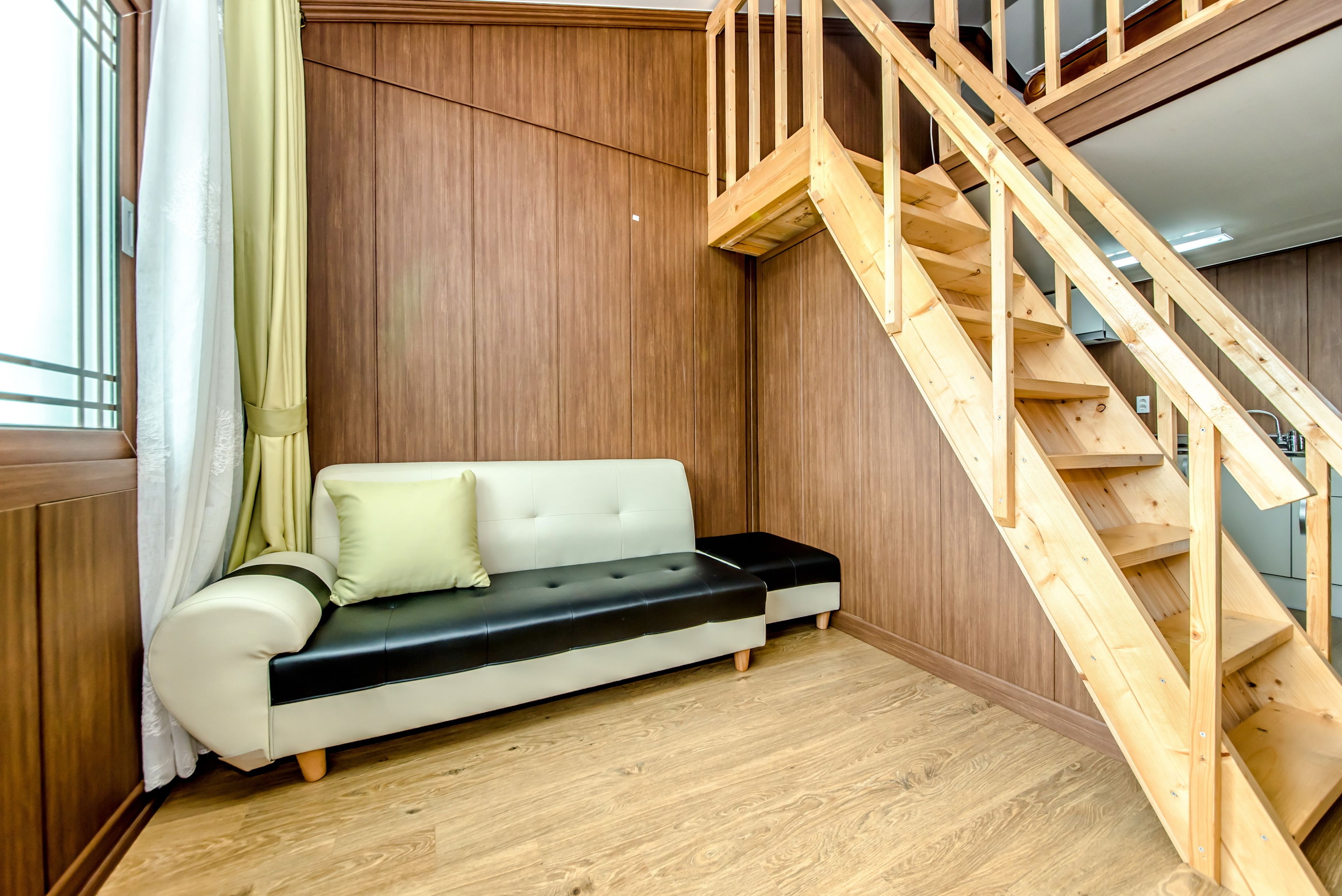 A wooden staircase leading to an upper level, a white sofa with a black seat cushion, and a wooden floor.