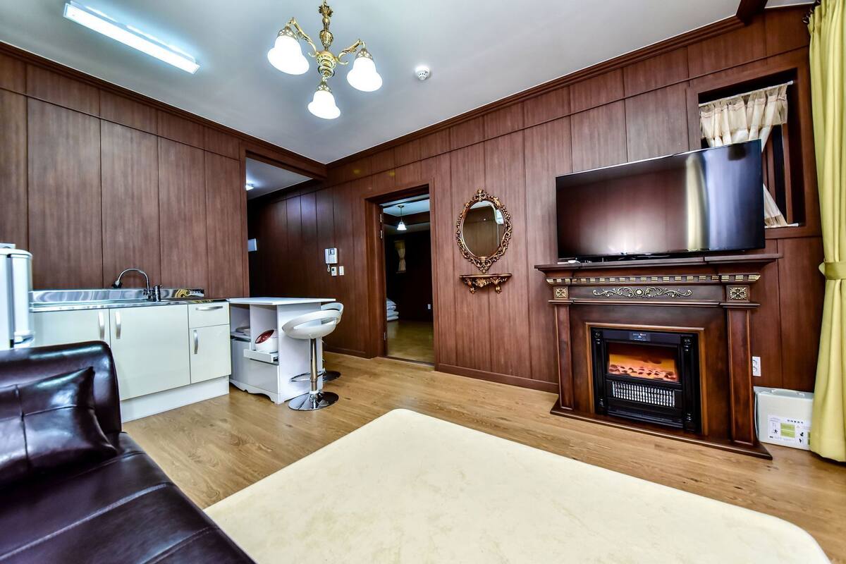 A living room with a fireplace, a television, a kitchen area, and a dining area.
