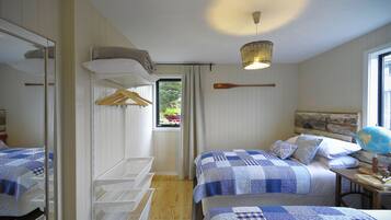 A bedroom with two beds, a wooden floor, a hanging light fixture, and a window with a view of greenery.