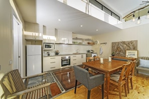 A modern kitchen with white cabinets, a wooden dining table, and a glass-top table. - Coastal Pods Wynyard (Wynyard)