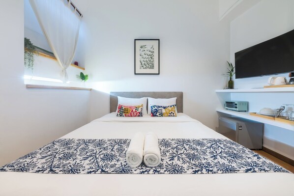 A hotel room with a bed, pillows, a flat-screen TV, a small fridge, and a window with a curtain. - Lee's Mark Residence (Samut Prakan)