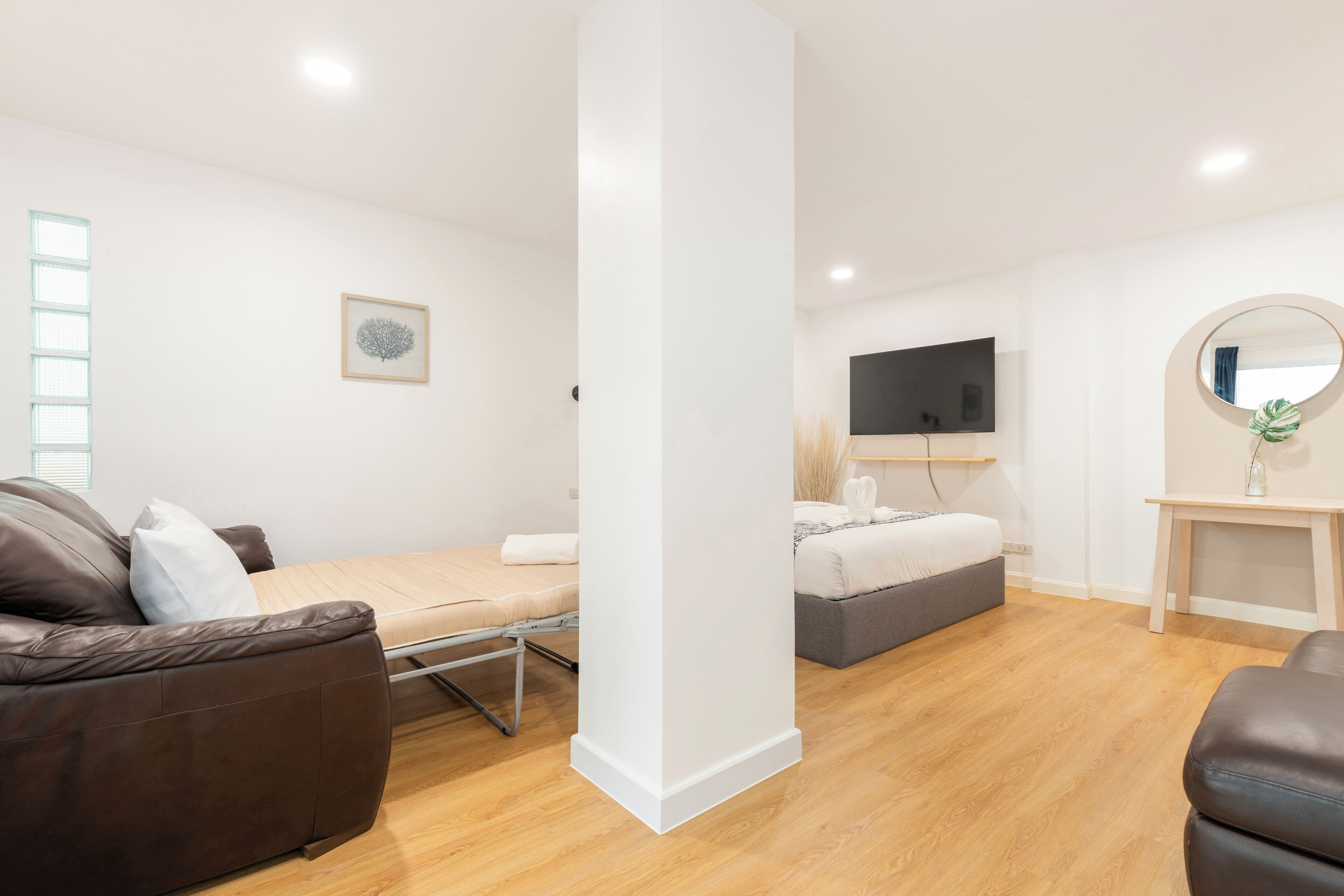Una sala moderna con sofá, cama, televisor y un espejo redondo.