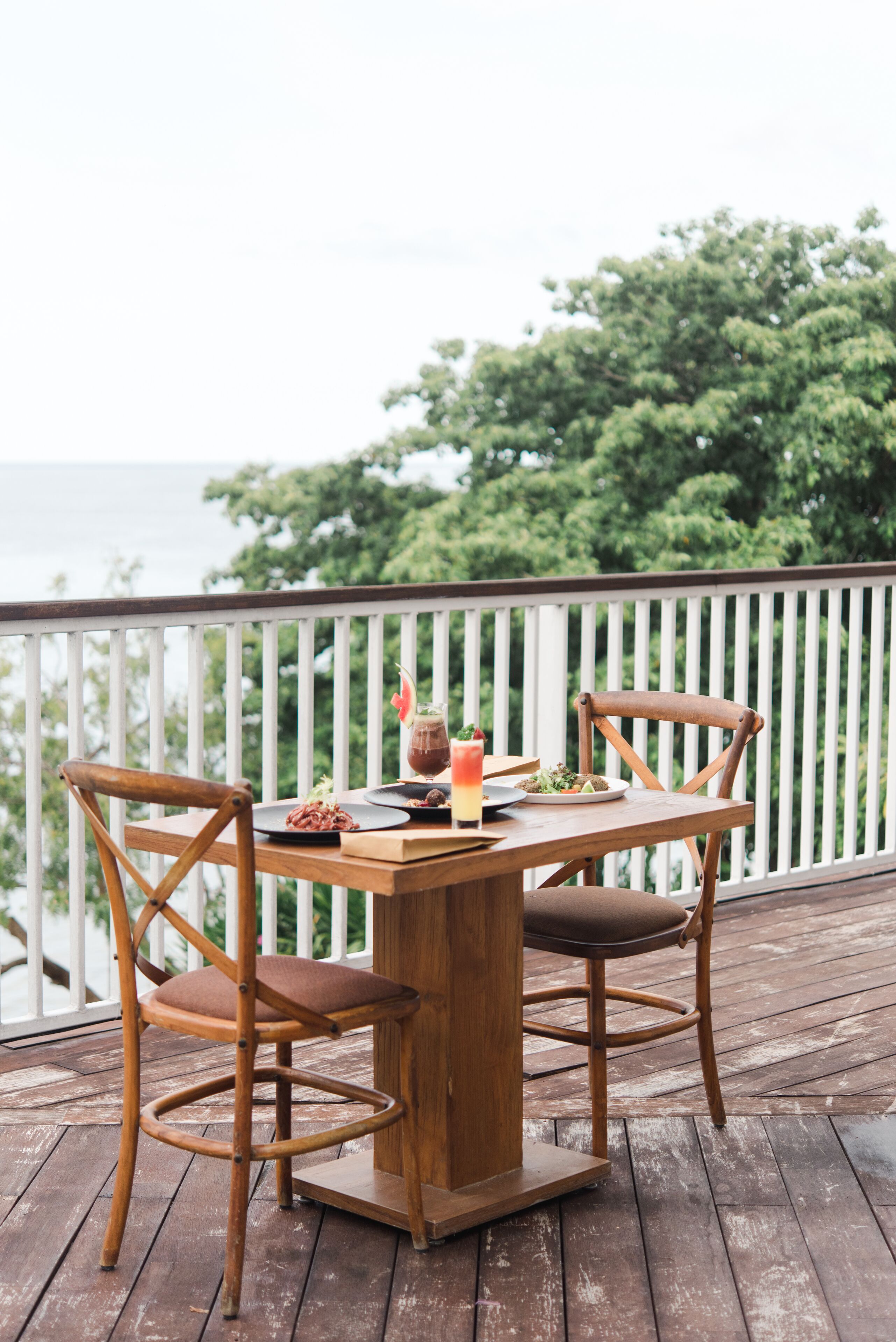 A wooden deck with a table and chairs, a glass of drink, and a plate of food.