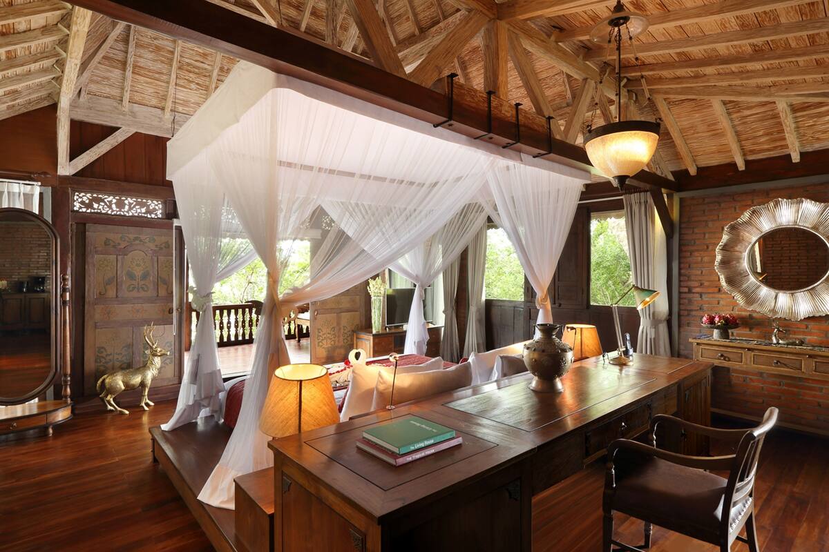 Une pièce avec un plafond en bois, un lit à baldaquin blanc, une table à manger avec des chaises et un grand miroir au mur.