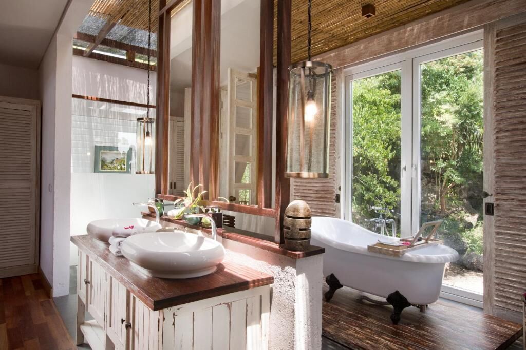 A bathroom with a large window, a bathtub, and a wooden vanity.