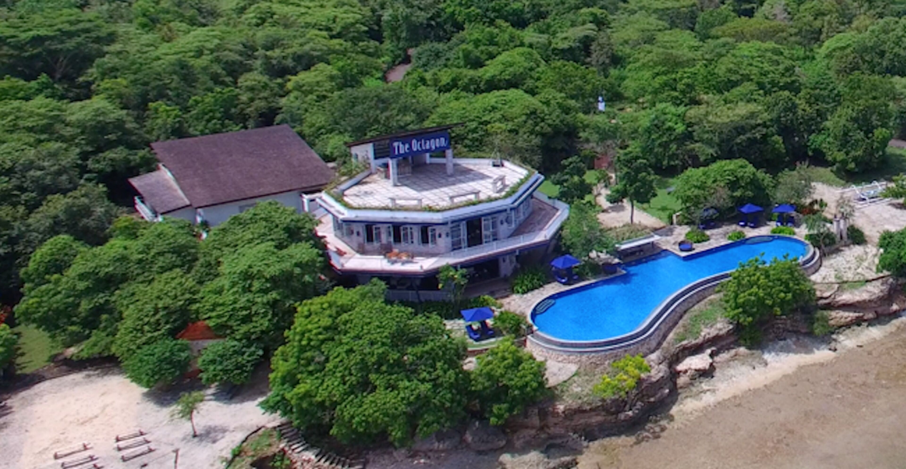 An aerial view of a resort with a swimming pool, a building labeled "The Octagon," and lush greenery surrounding the property.