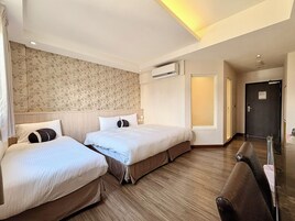 Quarto de hotel com duas camas, piso de madeira, papel de parede estampado, unidade de ar condicionado e uma porta.