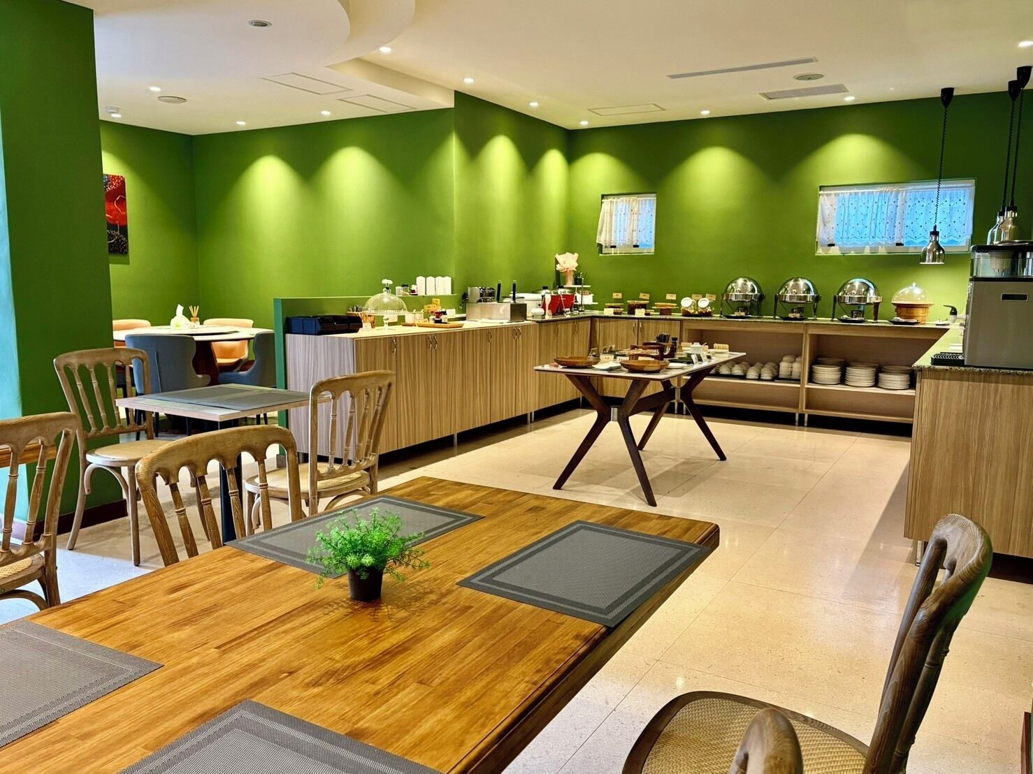 A modern dining area with green walls, wooden furniture, and a central table with a plant.