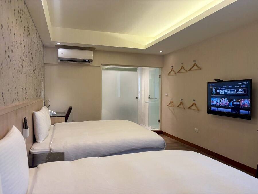 A hotel room with two beds, a TV mounted on the wall, and a door leading to a bathroom.