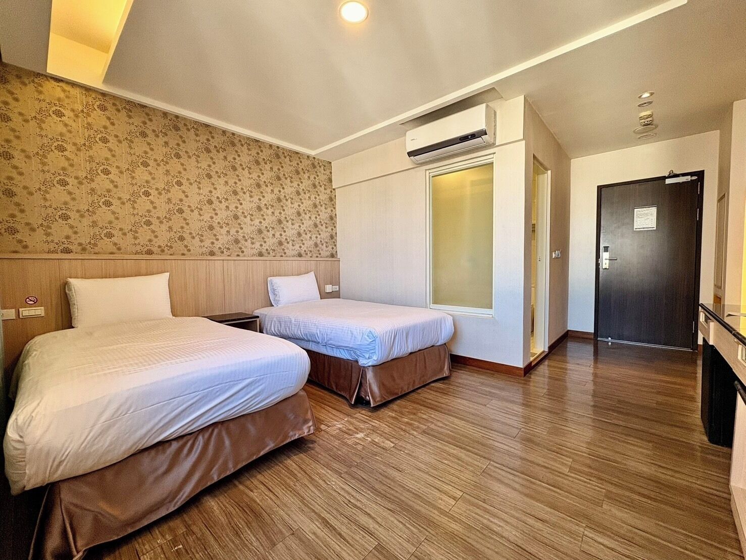 Una habitación de hotel con dos camas, un armario, un equipo de aire acondicionado y una puerta.