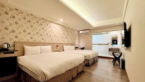 Habitación de hotel con dos camas, piso de madera, papel tapiz floral, televisión y baño visible a través de una puerta de vidrio.
