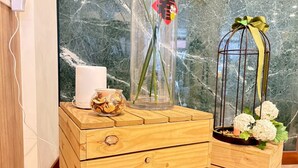 Un aparador de madera con una vela blanca, un florero de vidrio con tallos verdes y una jaula de metal con flores blancas.