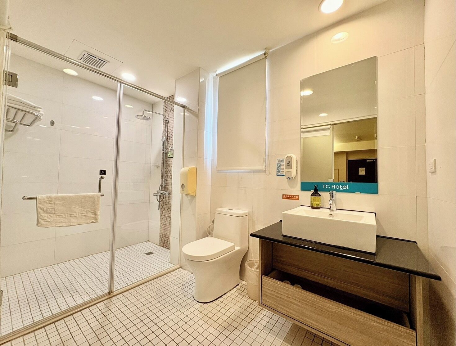 A hotel bathroom with a glass-enclosed shower, a toilet, and a vanity with a mirror.