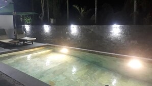 An outdoor swimming pool at night with stone walls and a bench. - Rice Field Homestay (Da Nang)