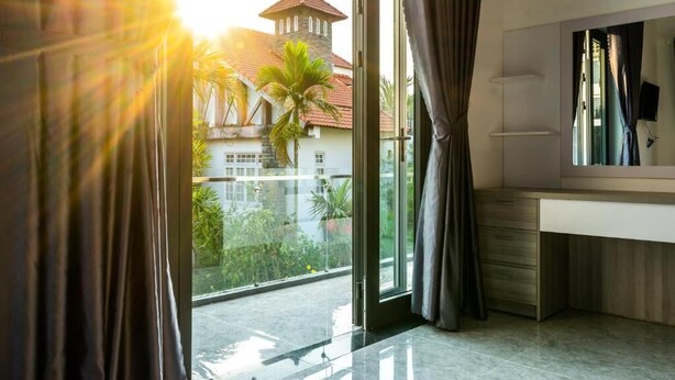 A modern bathroom with a large mirror, a vanity, and a view of a building with a tower and palm trees. - Rice Field Homestay (Da Nang)