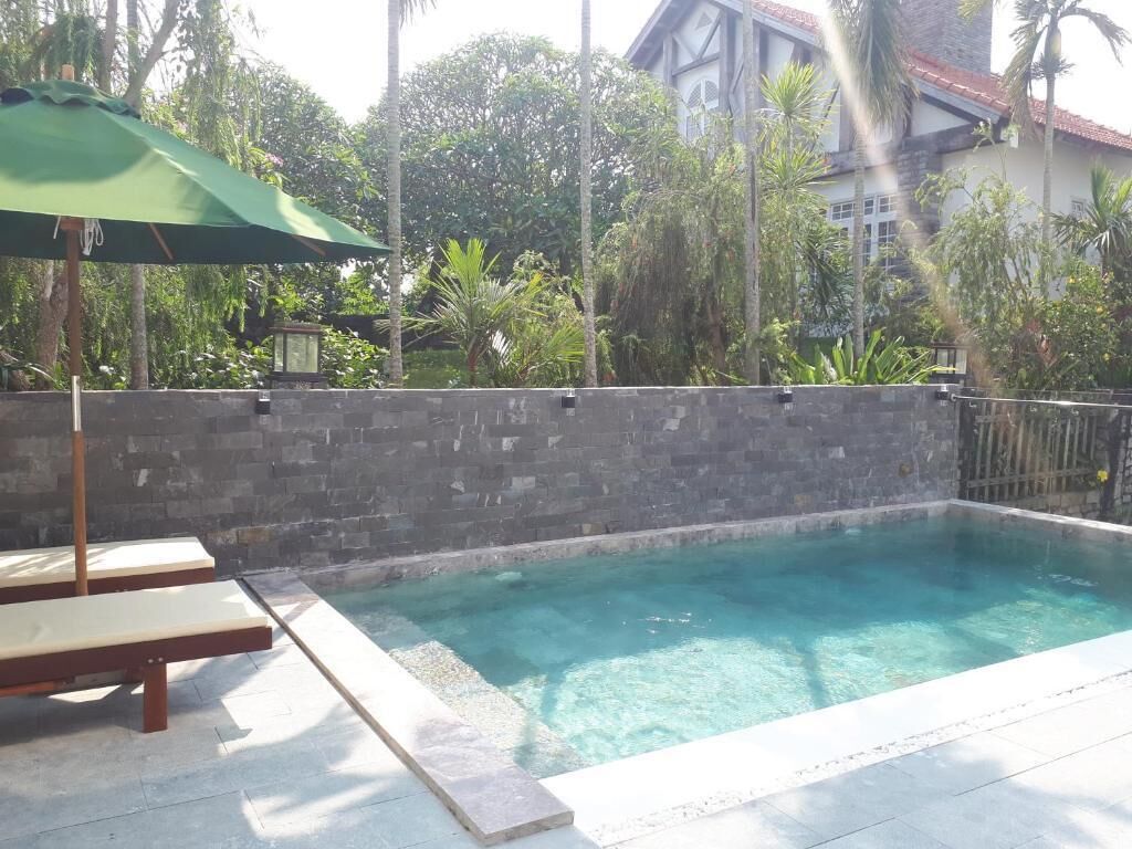 A swimming pool with a stone wall, a bench, and an umbrella.