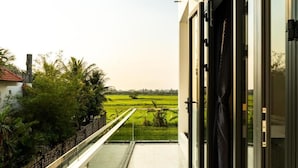 A balcony with a view of a green field and a building with a red roof. - Rice Field Homestay (Da Nang)