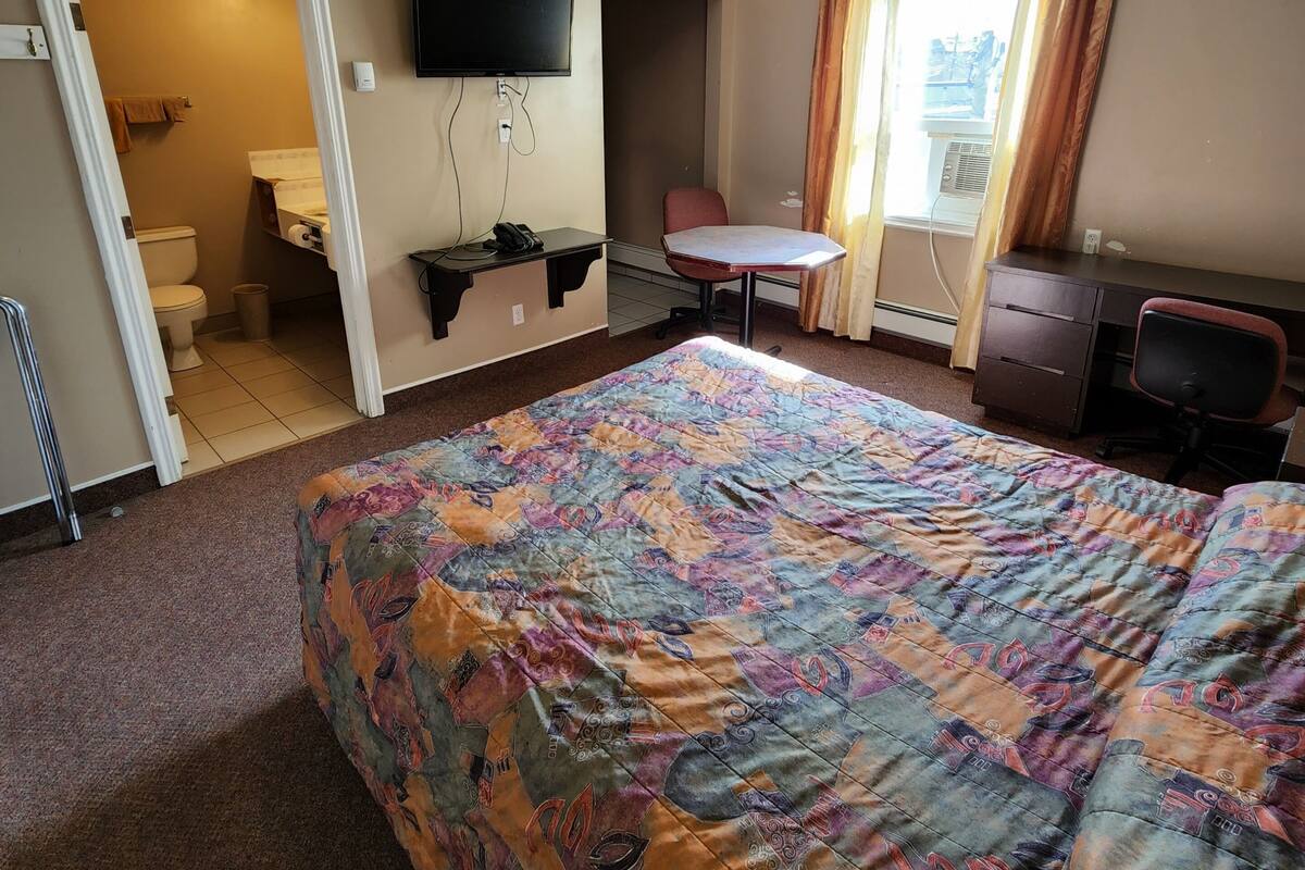 A hotel room with a large bed, a desk, a chair, a television, and a bathroom visible through an open door.