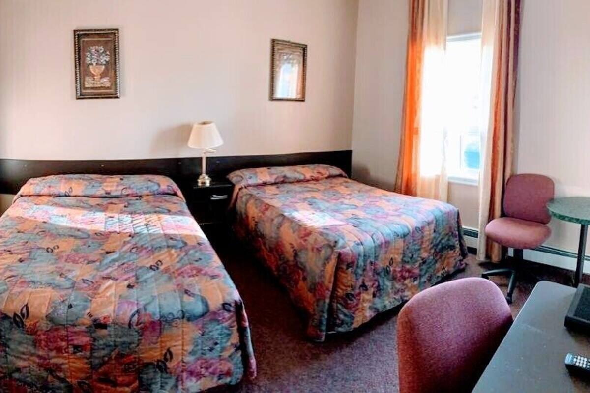 A hotel room with two beds, a desk, a chair, and a lamp.