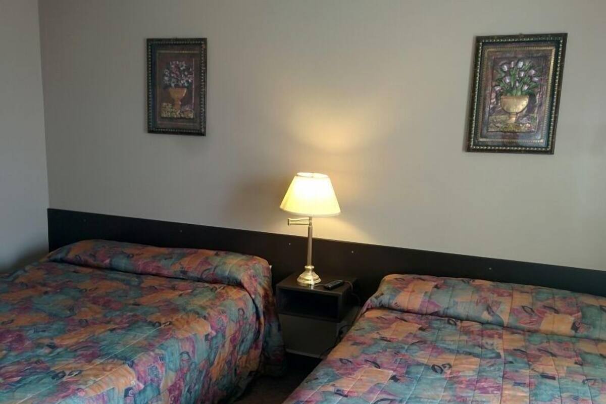 A hotel room with two beds, a nightstand with a lamp, and two framed pictures on the wall.