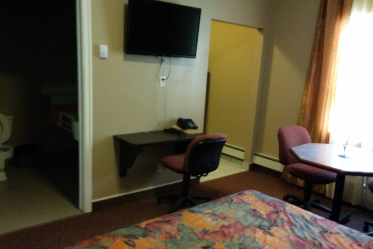 A hotel room with a bed, a desk, a chair, a television, and a window with curtains.