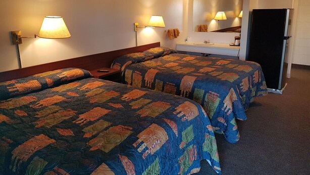Hotellihuone, jossa on kaksi sänkyä, lipasto, peili, jääkaappi ja seinään kiinnitetyt lamput.