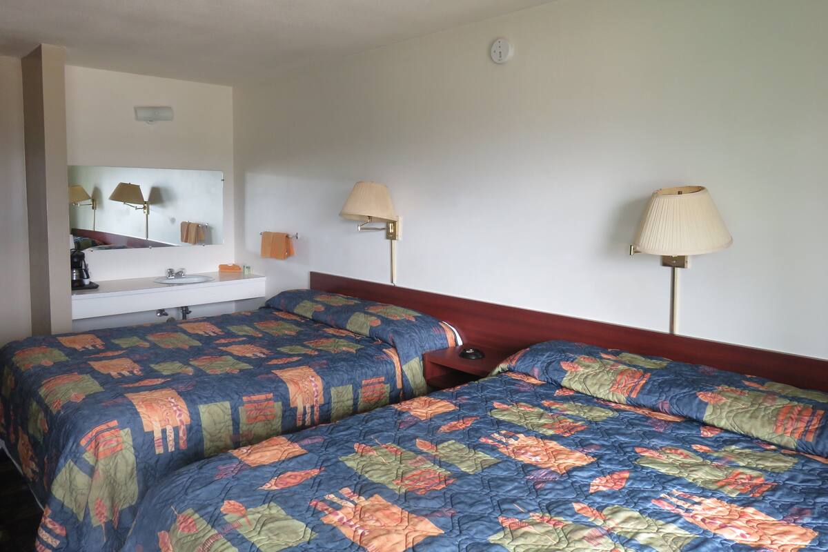 Une chambre d’hôtel avec deux lits, une salle de bain avec un lavabo et deux lampes fixées au mur.