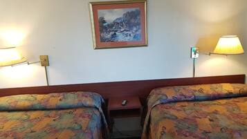 Quarto de hotel com duas camas, um quadro na parede e duas luminárias fixadas na parede.