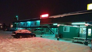 Rakennus, jossa on katettu ulkoalue, lumessa parkkeerattu auto ja piknikpöytä.