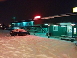 A building with a covered outdoor area, a car parked in the snow, and a picnic table.