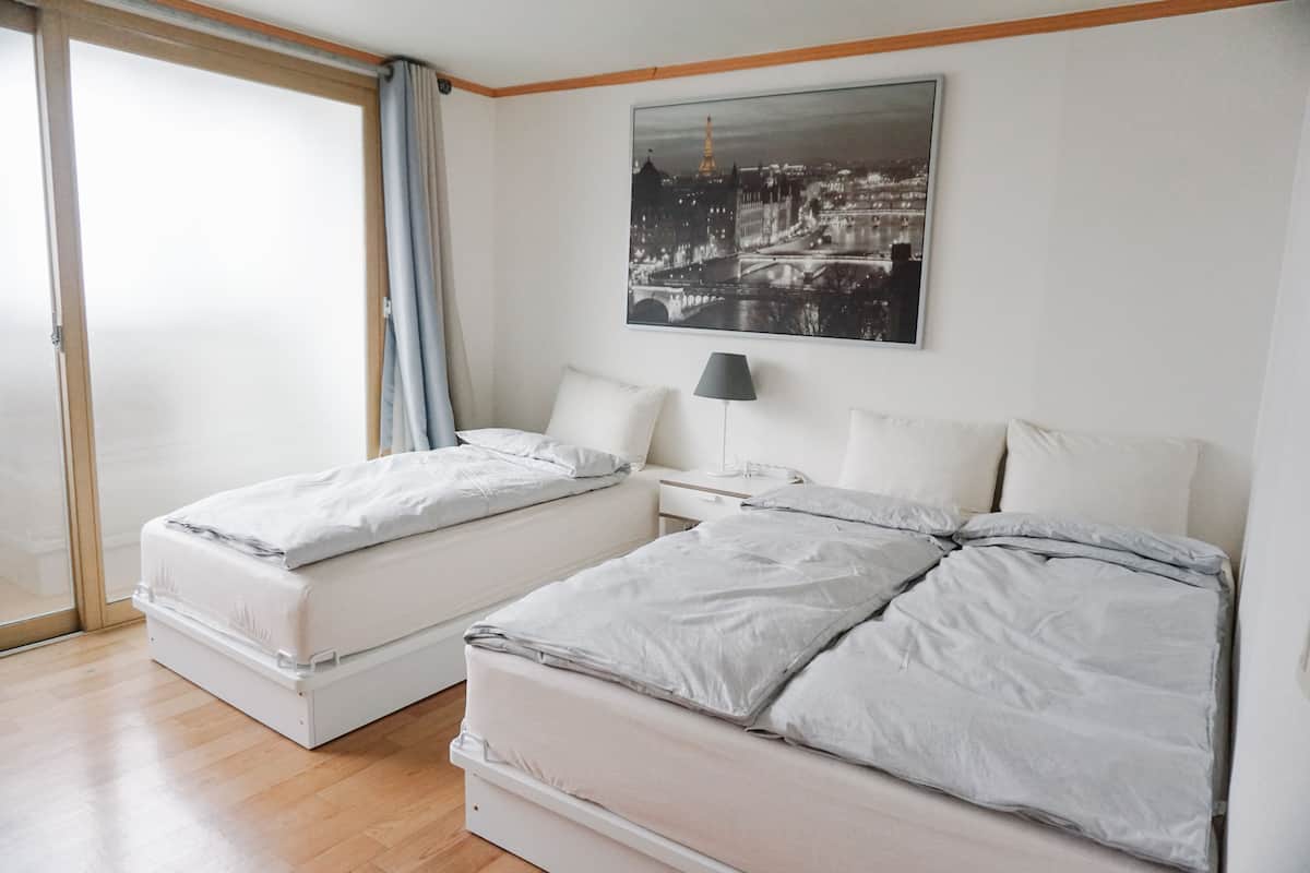 Ein Hotelzimmer mit zwei Betten, einem Nachttisch, einer Lampe und einem Stadtbild an der Wand.