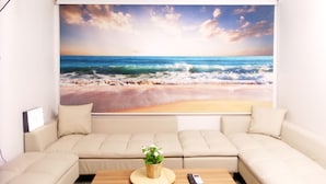 A living room with a large beach mural, a beige sofa, a small wooden table, and a single potted plant. - Hongdae Lai Lai house (Seoul)