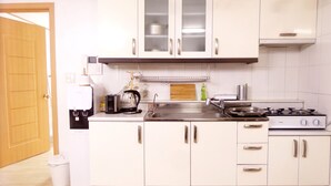 A compact kitchen with white cabinets, a coffee maker, a kettle, a stove, and a sink. - Hongdae Lai Lai house (Seoul)
