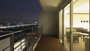 Un balcón con vista a un paisaje urbano nocturno, con un ventanal de vidrio que da a una habitación con un sofá y una mesa.