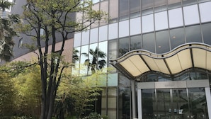 Un edificio moderno con fachada de vidrio, vestíbulo cubierto y zonas verdes circundantes.