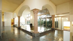 Amplia zona de piscina interior con techo alto, suelo de baldosas y varios arcos.