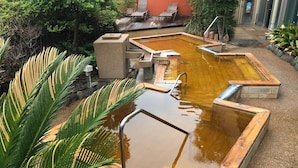 Un área de aguas termales con varias piscinas, escalones de madera y barandillas de piedra.
