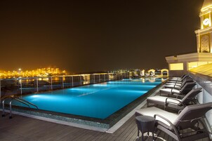 Piscina noturna com espreguiçadeiras e vista para o horizonte urbano.