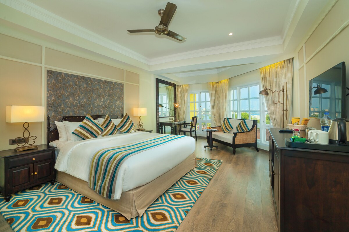 A hotel room with a large bed, a desk, a chair, a television, and a ceiling fan.