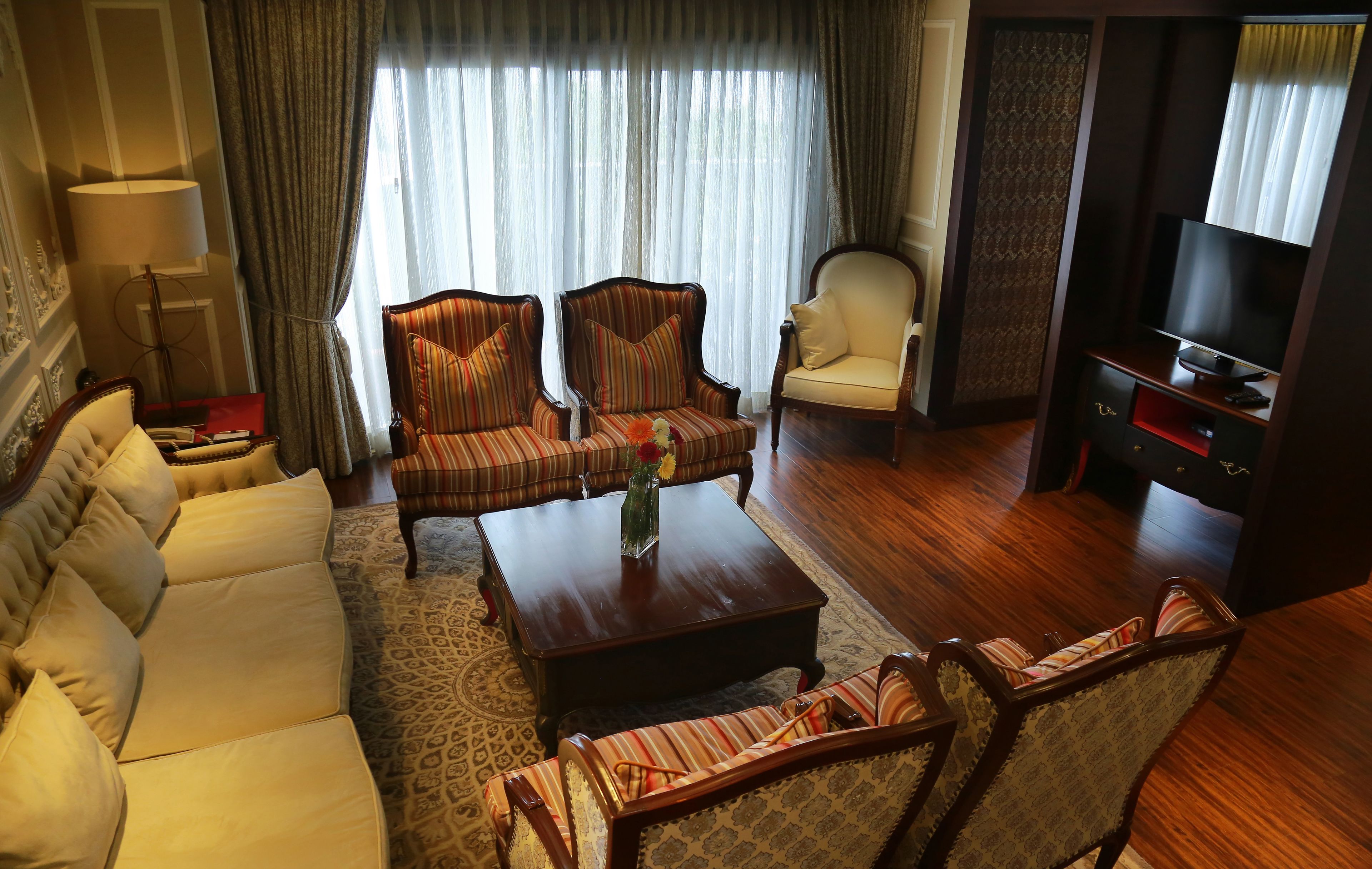Hotelkamer met een sofa, twee fauteuils, een salontafel, een tv-meubel en een kamerbreed tapijt met dessin.