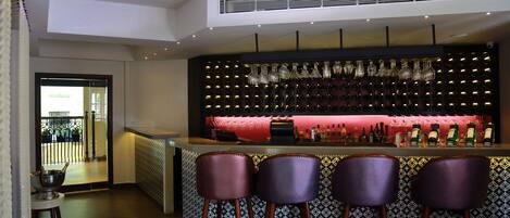 A bar area with a red counter, multiple bottles, and three bar stools.