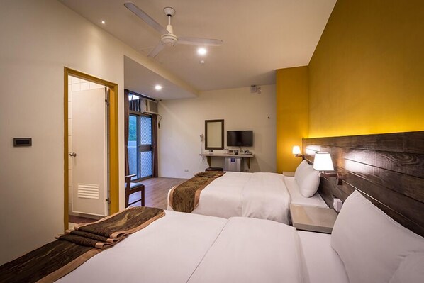 A hotel room with two beds, a desk with a computer, a ceiling fan, and a view of a balcony. - An Tong Hot Spring Hotel (Yuli)