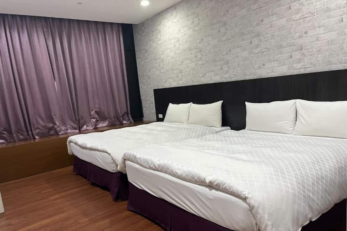 A hotel room with a large bed, a wooden floor, a brick wall, and a window with curtains.