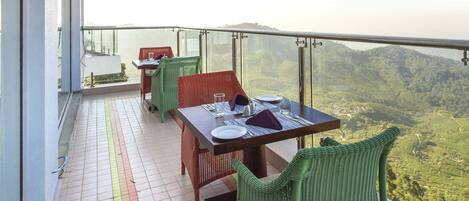 Un balcon avec une table et des chaises, un sol carrelé avec une ligne de sécurité, et une vue panoramique sur un paysage montagneux.