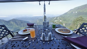 Mesa servida con platos, cubiertos, vasos y una botella, con vistas a un paisaje montañoso.