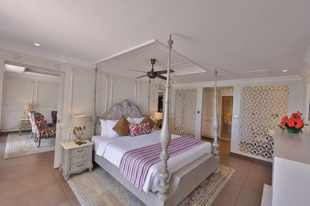 A spacious bedroom with a four-poster bed, a ceiling fan, and a decorative wall panel.