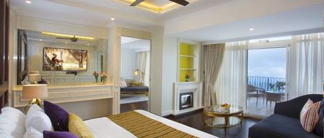 A hotel room with a bed, a sofa, a fireplace, a balcony with a view, and a ceiling fan.